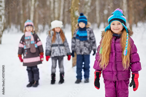 Smiling little girl stands in winter park, her friends stand
