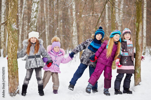 Children play in winter park tugging hands between two trees