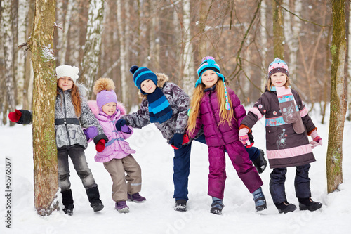 Five children play in winter park tugging hands between two tree
