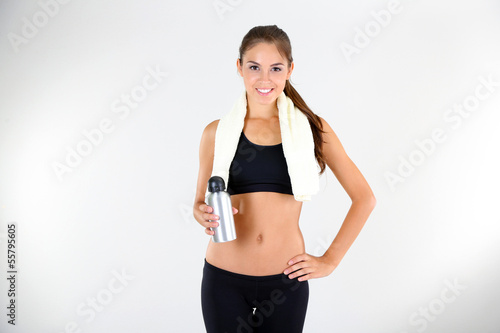 Beautiful young girl with bottle of water on light background