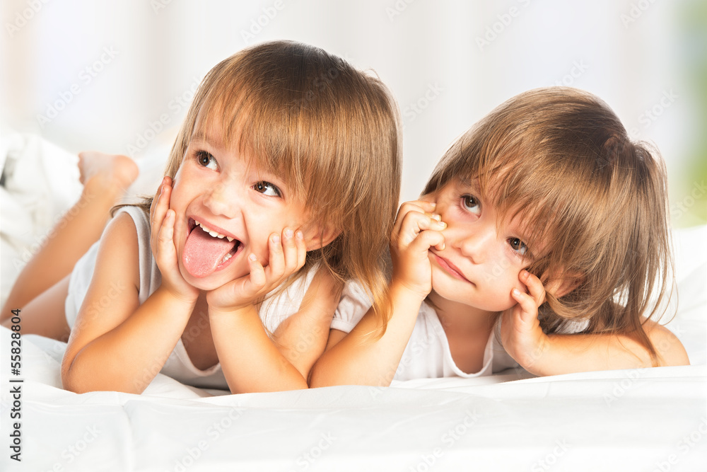 happy little girls twins sister in bed under the blanket having happy little girls twins sister in bed under the blanket having