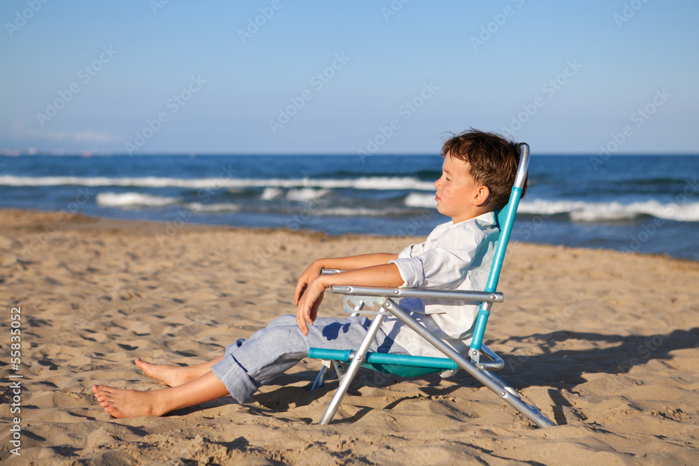 Thoughtful boy sitting on chair at beach