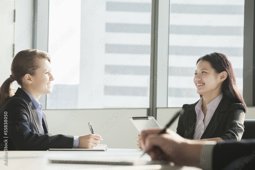 Two businesswomen smiling and looking at each other during a business meeting Two businesswomen smiling and looking at each other during a business meeting