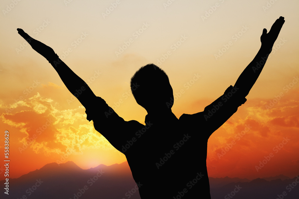 Silhouette of young man with arms raised with a beautiful sunset and landscape in the background Silhouette of young man with arms raised with a beautiful sunset and landscape in the background