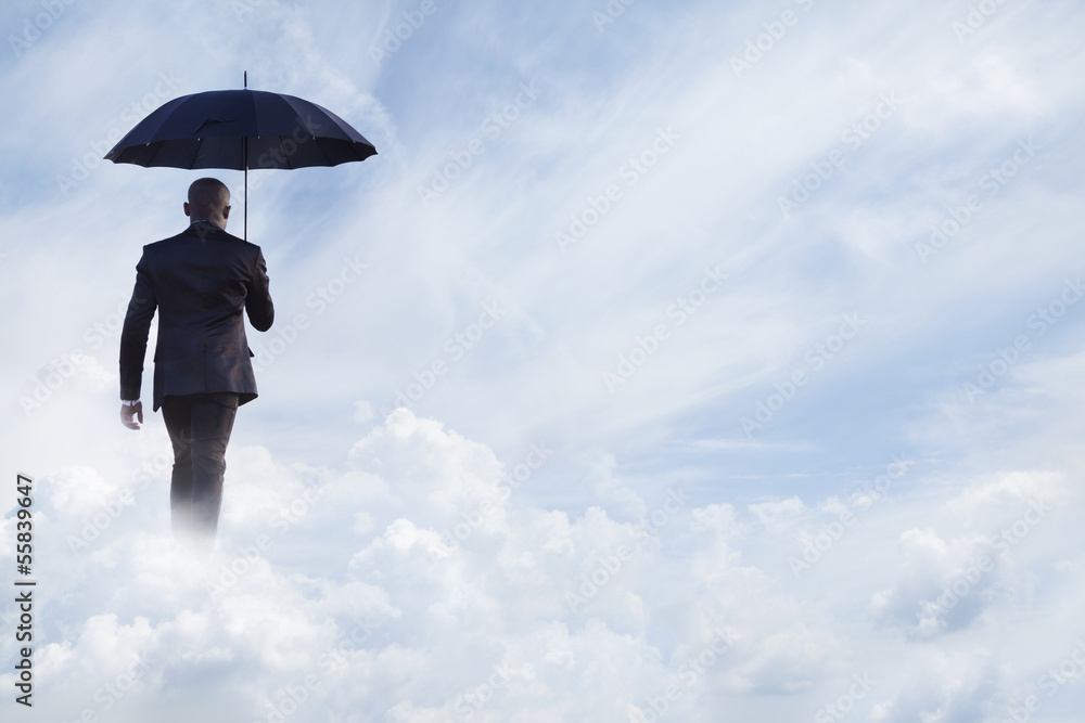 Businessman holding an umbrella and walking away in dreamlike clouds Businessman holding an umbrella and walking away in dreamlike clouds