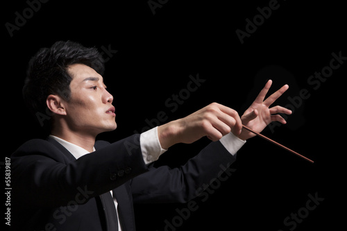 Young conductor with baton raised, black background photo
