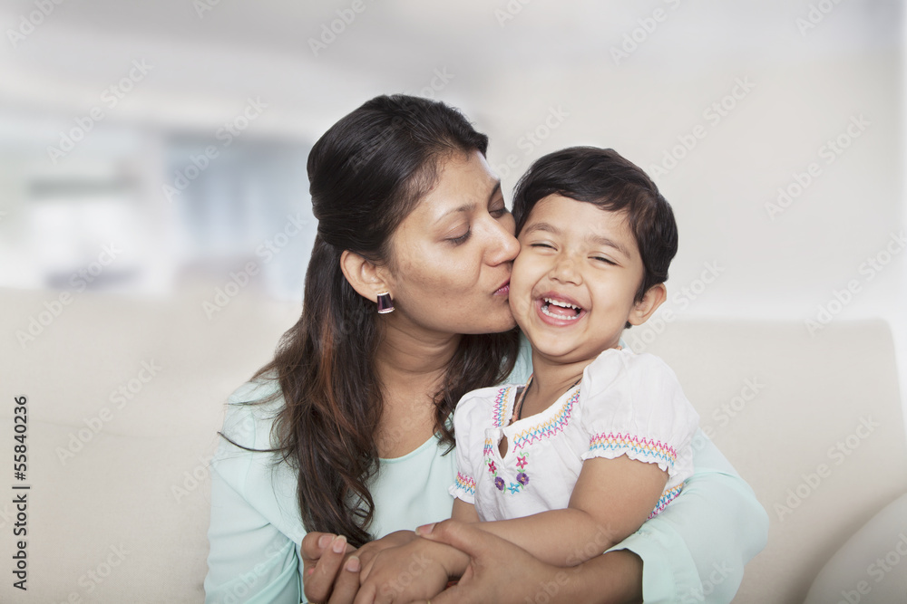 Affectionate mother holding and kissing her daughter on the couch Affectionate mother holding and kissing her daughter on the couch