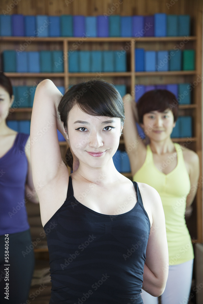 Three young women stretching and doing yoga, looking at camera, 