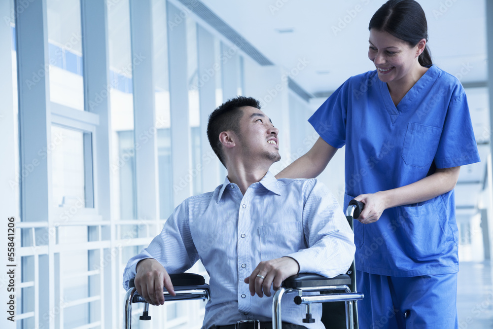 Smiling female nurse pushing and assisting patient in a wheelchair in the hospital Smiling female nurse pushing and assisting patient in a wheelchair in the hospital
