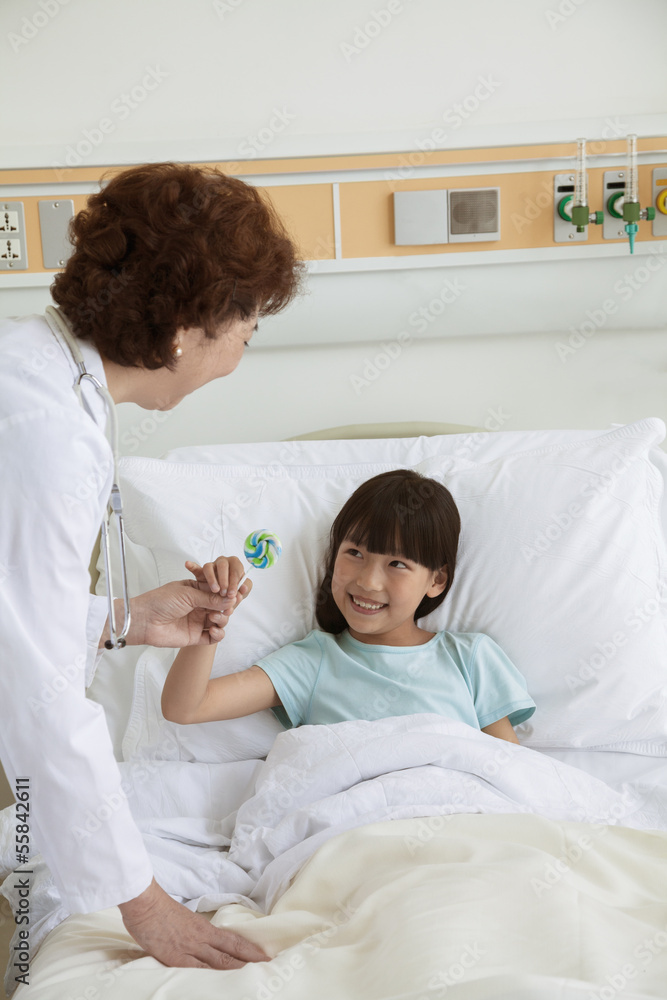 Obraz premium Female doctor giving a lollipop to a young girl lying in a hospital bed