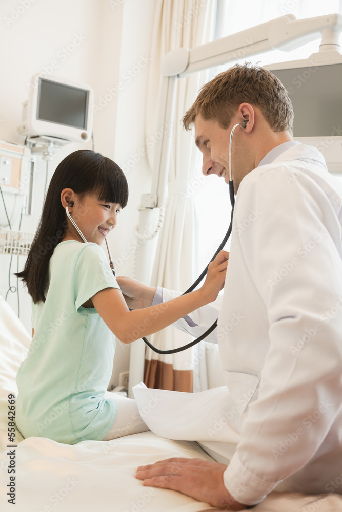 Fototapeta premium Girl patient checking the doctors heart beat with a stethoscope on a hospital bed
