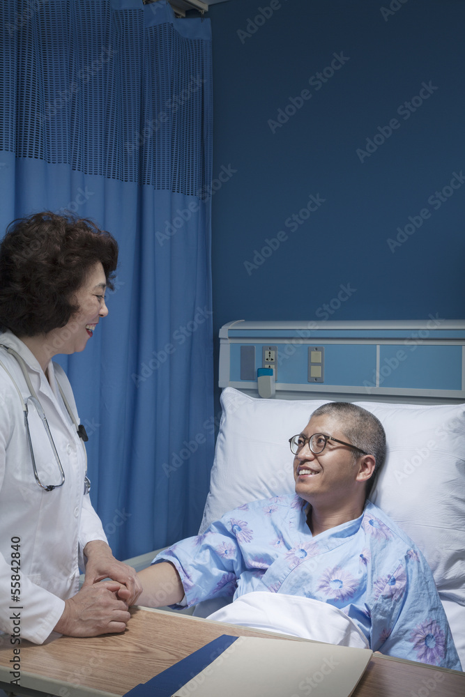 Obraz premium Smiling doctor checking up on a patient lying down in a hospital bed, holding hands