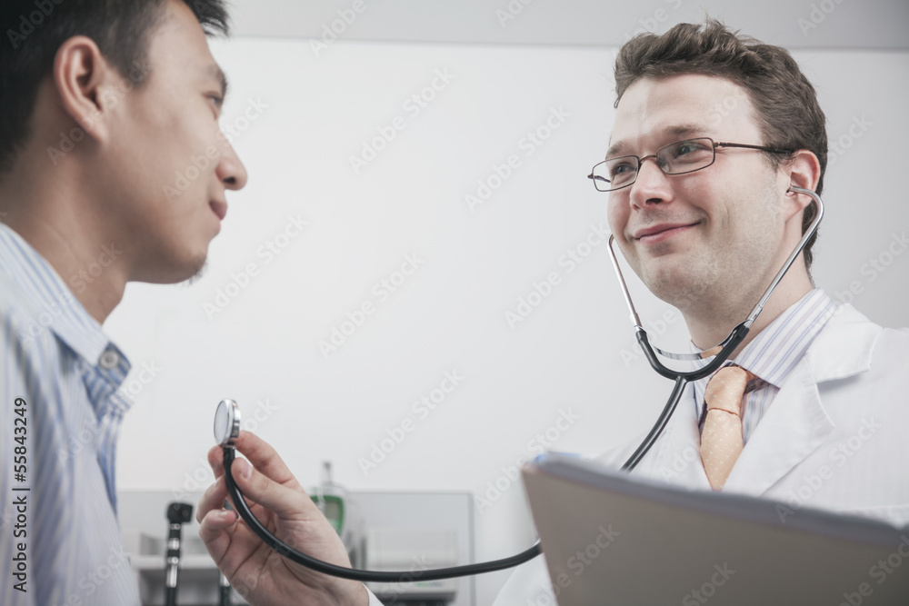Smiling doctor checking heartbeat of a patient with a stethoscope Smiling doctor checking heartbeat of a patient with a stethoscope
