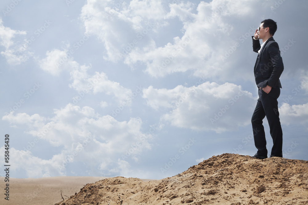 Young businessman in sunglasses standing in the desert and talking on the phone Young businessman in sunglasses standing in the desert and talking on the phone