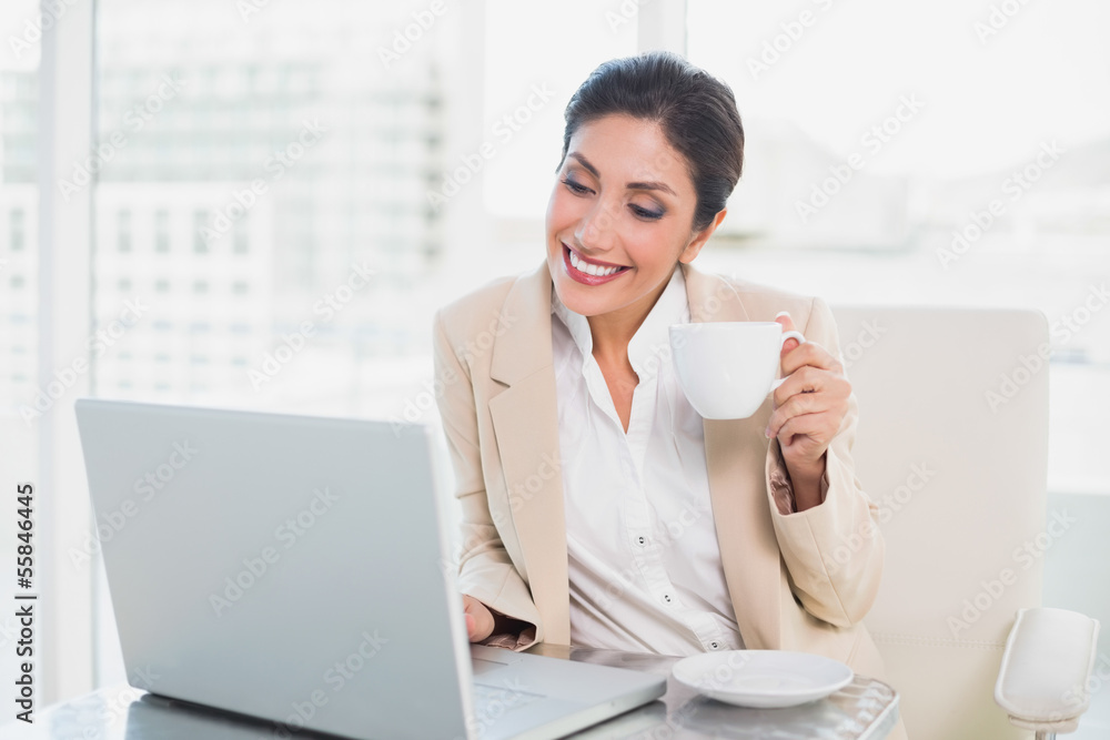 Happy businesswoman holding cup while typing on laptop Happy businesswoman holding cup while typing on laptop