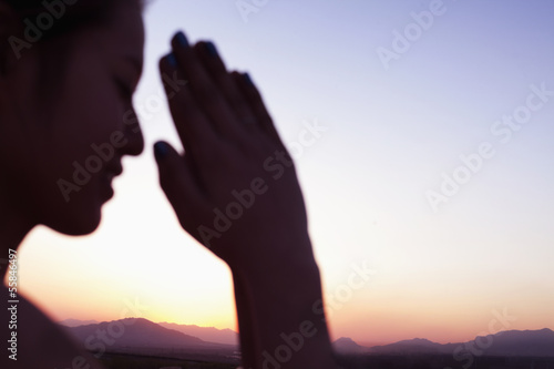 Serene young woman with eyes closed and hands together in prayer pose in the desert in China, focus on background