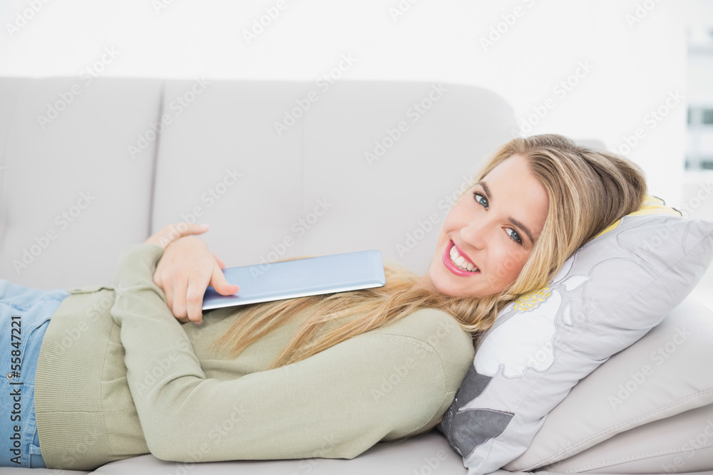 Cheerful pretty blonde holding her tablet lying on cosy sofa Cheerful pretty blonde holding her tablet lying on cosy sofa
