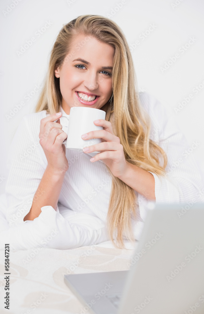 Smiling pretty model holding coffee lying on cosy bed Smiling pretty model holding coffee lying on cosy bed