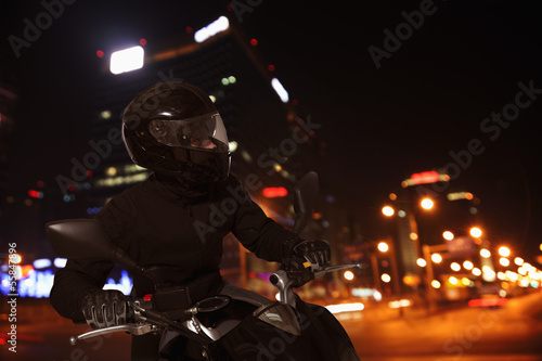 Young Man riding a motorcycle at night through the streets of Beijing © xixinxing