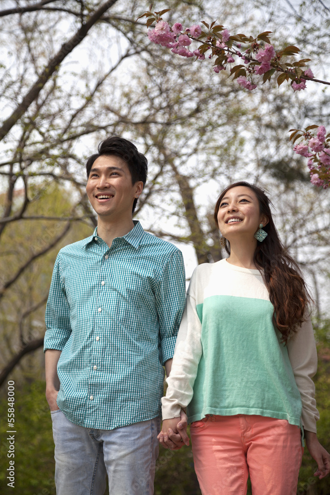 Happy smiling young couple holding hands in the park in springtime, three quarter length Happy smiling young couple holding hands in the park in springtime, three quarter length