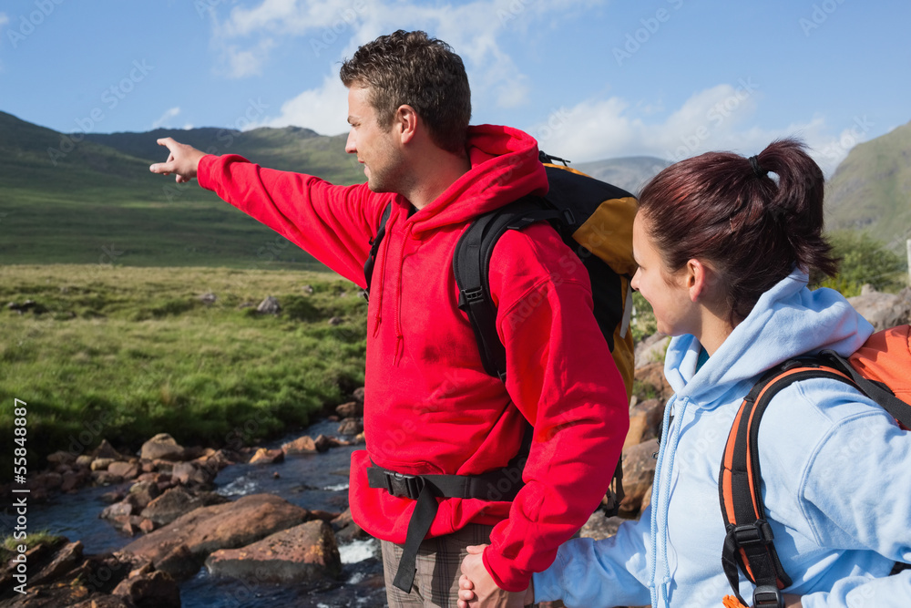 Couple standing at edge of river on a hike with man pointing