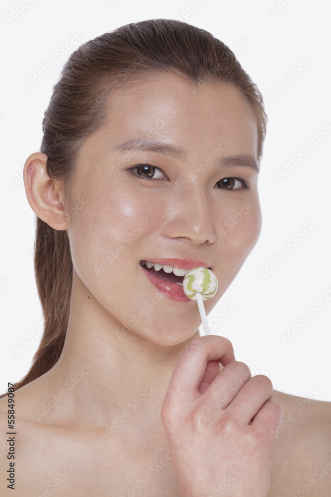 Smiling young woman looking into camera and licking a lollipop, studio shot Smiling young woman looking into camera and licking a lollipop, studio shot