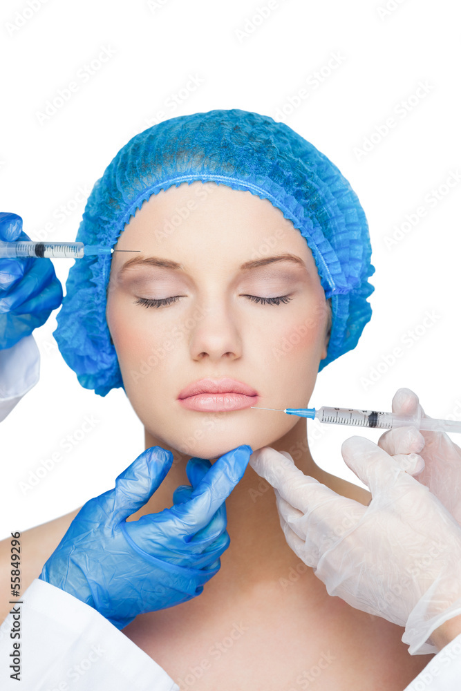 Surgeons injecting young woman wearing blue surgical cap Surgeons injecting young woman wearing blue surgical cap