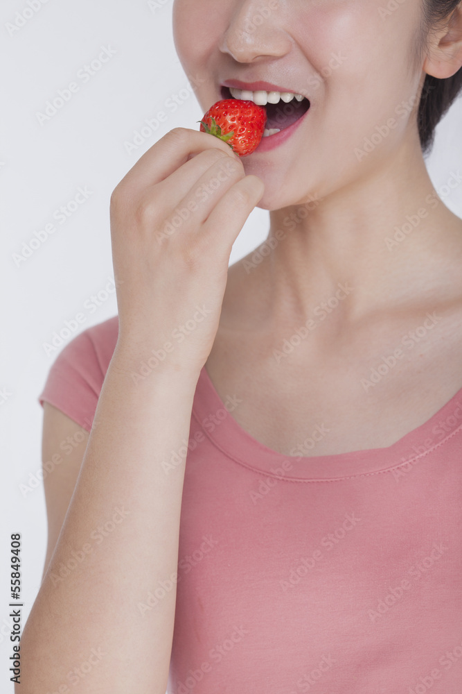 Young woman in pink shirt eating a strawberry, studio shot, half face showing Young woman in pink shirt eating a strawberry, studio shot, half face showing