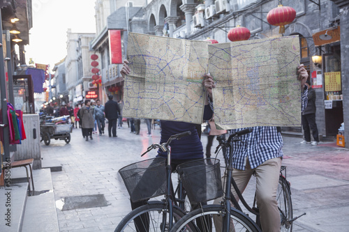 Young man and woman on bicycles holding maps.