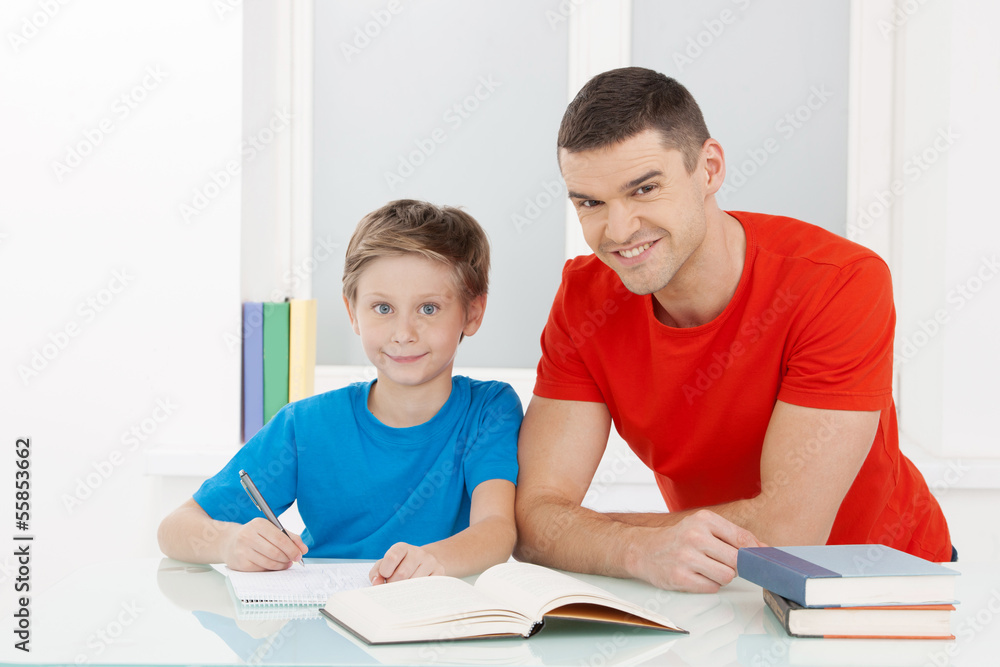 Father and son. Cheerful father helping his son with homework Father and son. Cheerful father helping his son with homework