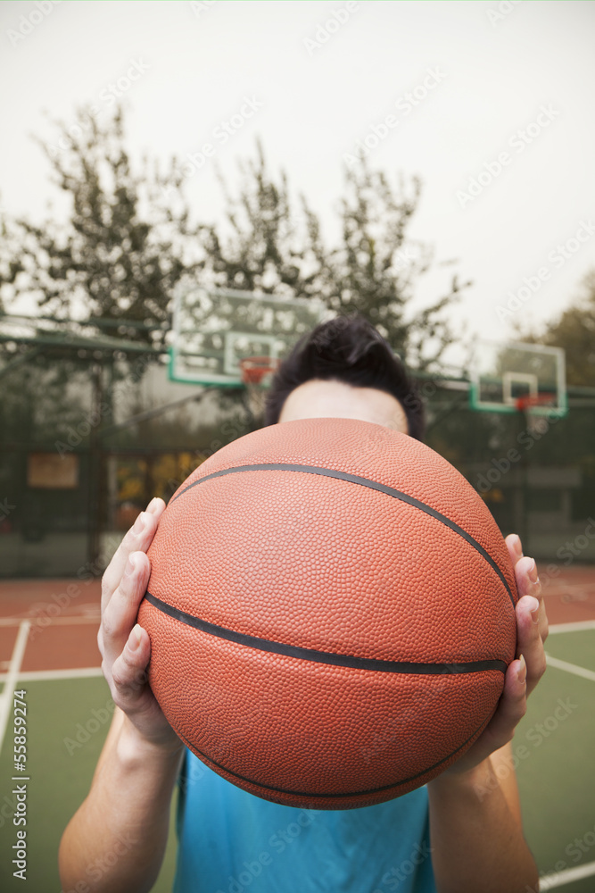 Young man covering his face with basketball, portrait Young man covering his face with basketball, portrait