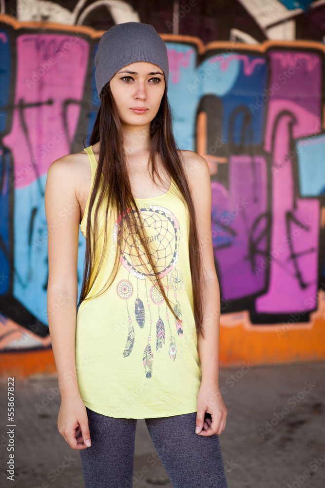 Naklejka premium Teenage girl with gray hat in front of graffiti wall