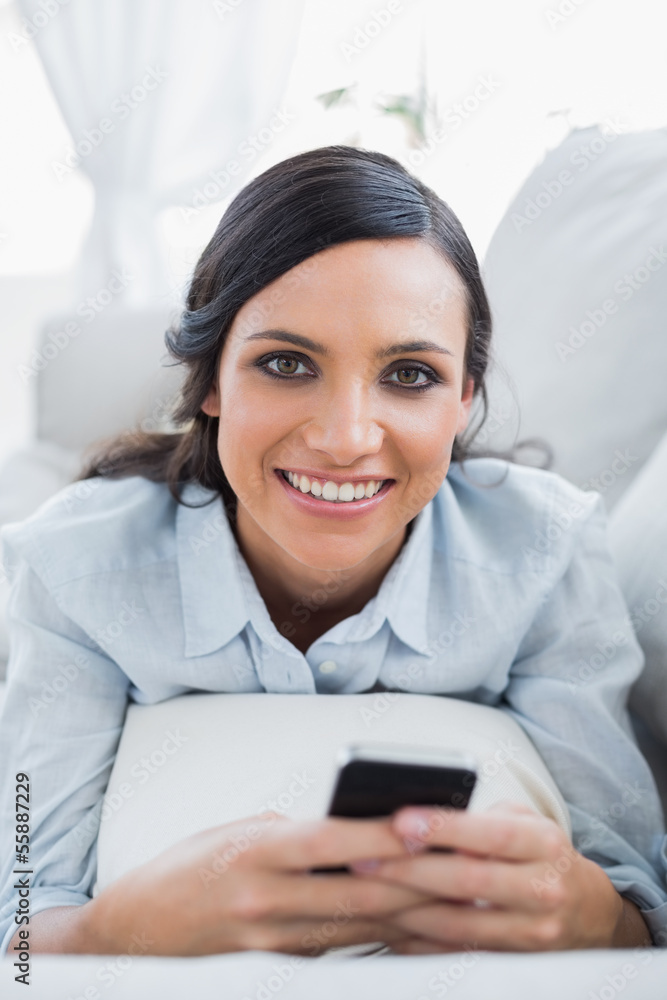 Cheerful pretty woman lying on the couch using her smartphone Cheerful pretty woman lying on the couch using her smartphone