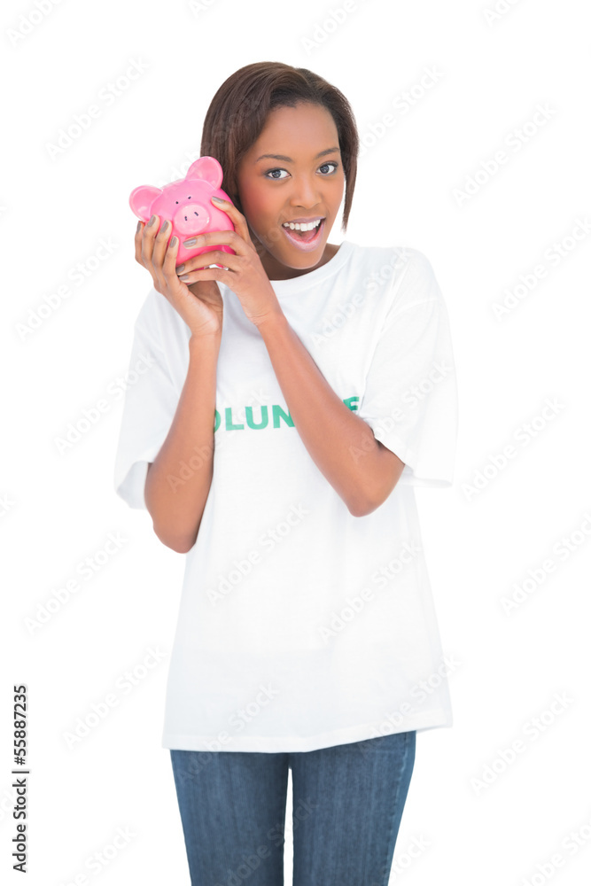Smiling woman shaking piggy bank by her ear Smiling woman shaking piggy bank by her ear
