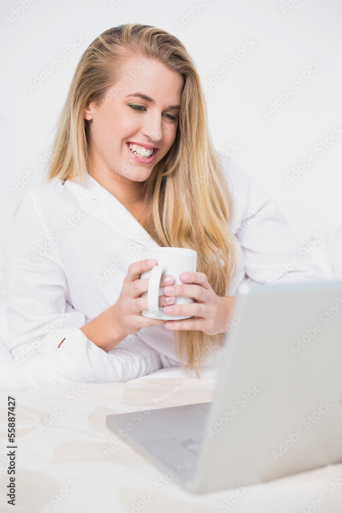 Happy pretty model looking at her laptop lying on cosy bed Happy pretty model looking at her laptop lying on cosy bed