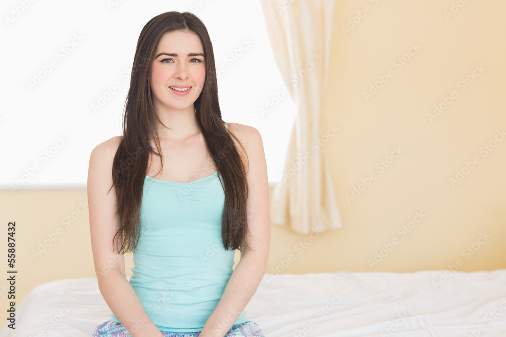 Long haired girl looking at camera sitting on her bed