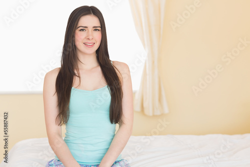 Long haired girl looking at camera sitting on her bed