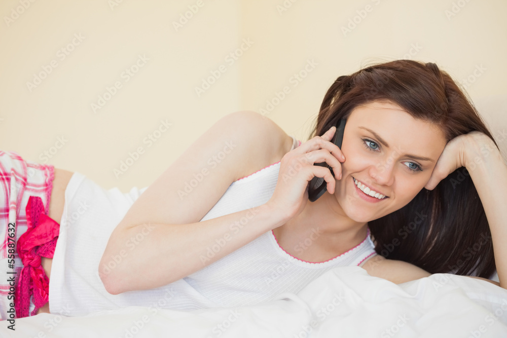 Smiling girl calling someone with a mobile phone lying on a bed Smiling girl calling someone with a mobile phone lying on a bed