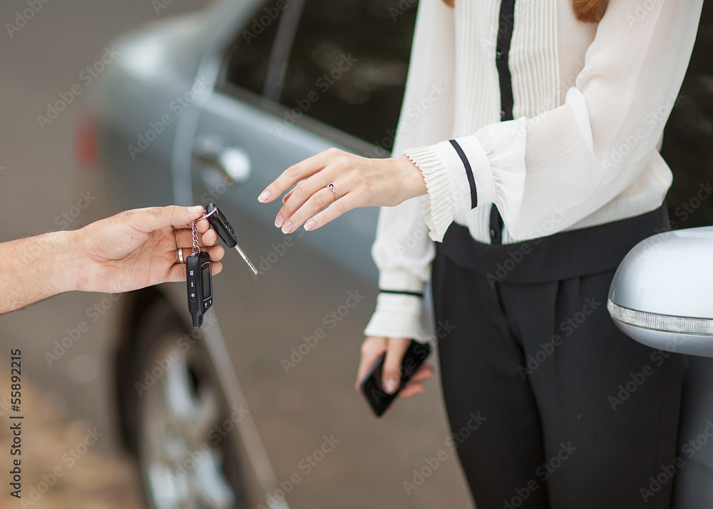 Male hand giving car key to female hand. She is holding a cell p