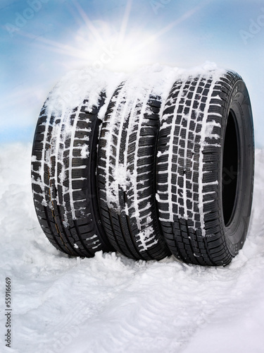 Snowy winter tyres in front of blue sky with sunlights