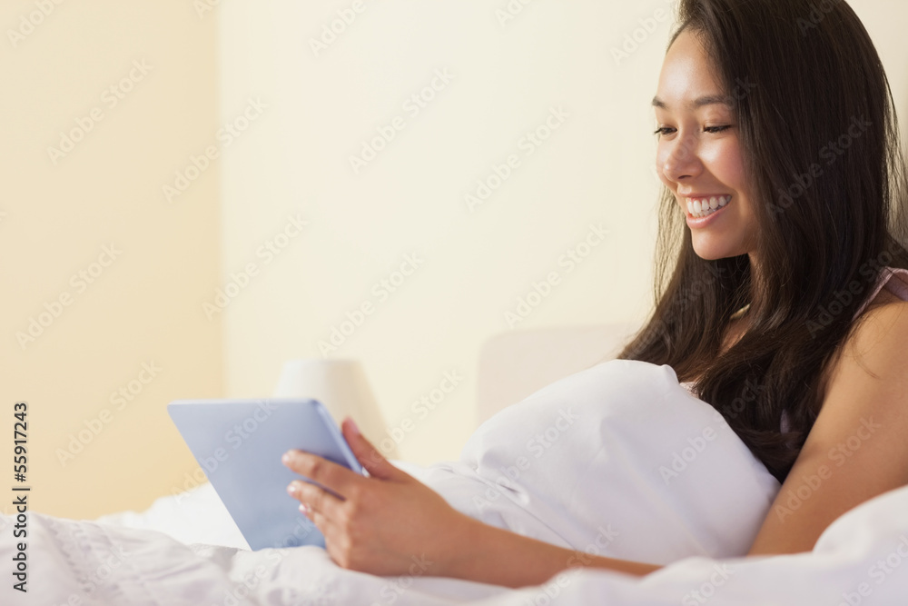 Happy young asian woman sitting in bed using tablet pc Happy young asian woman sitting in bed using tablet pc