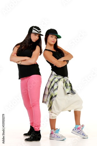Two confident brunettes in hip hop outfits standing back to back