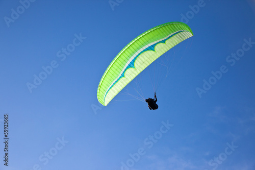 Green paraglider flying in blue sky.