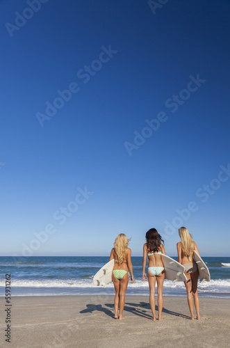 Three Beautiful Women Surfers In Bikinis With Surfboards At Beac