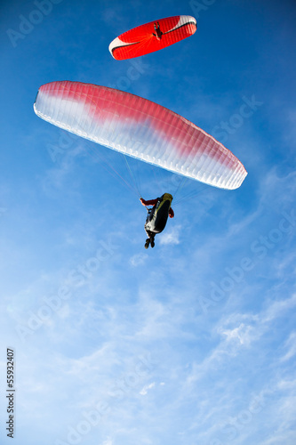 Two paragliders flying in blue sky.