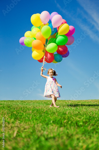 Little girl holding colorful balloons. Child playing on a green