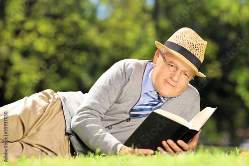 Senior gentleman lying on a grass with a book in park