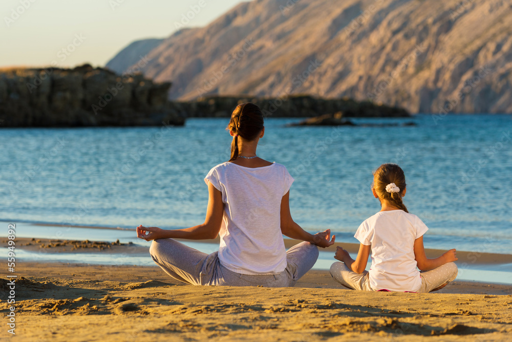 Mother and daughter doing yoga exercise on the beach