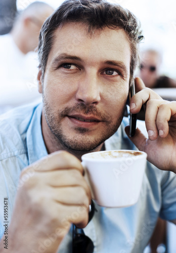 Young businessman talking on the phone and drinking coffee