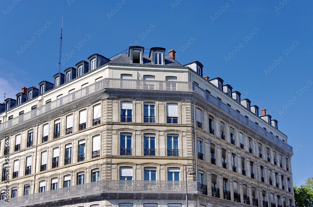 Immeuble de pierre blanche en coin, ciel bleu.